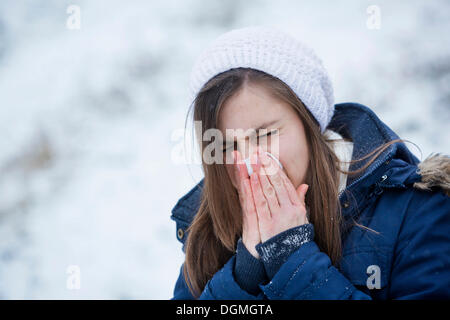 Giovane donna indossa abbigliamento invernale soffia il naso, Germania Foto Stock