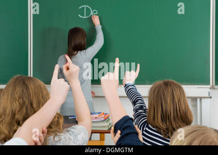 La scuola dei bambini alzando le braccia per rispondere durante la classe, Germania Foto Stock