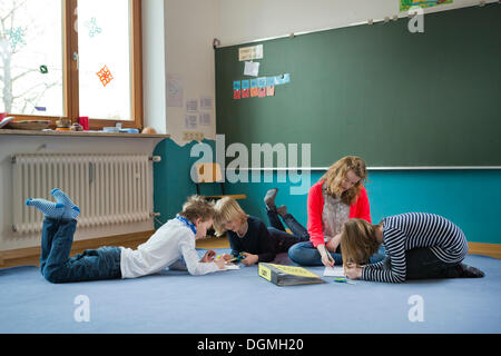 Gli studenti di una scuola indipendente seduto o disteso a lavorare sul terreno, Aktive Schule Peterhausen, Petershausen Foto Stock