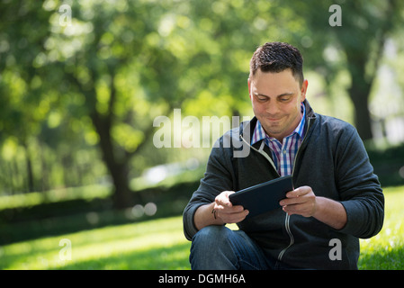 L'estate. La gente di affari. Un uomo seduto utilizzando una tavoletta digitale, mantenendo in contatto. Foto Stock