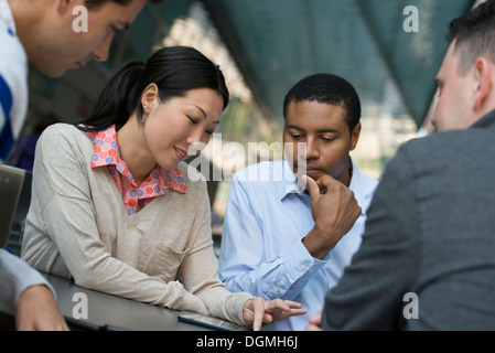 La gente di affari in movimento. Quattro persone raccolte intorno a una tavoletta digitale avente una discussione. Foto Stock