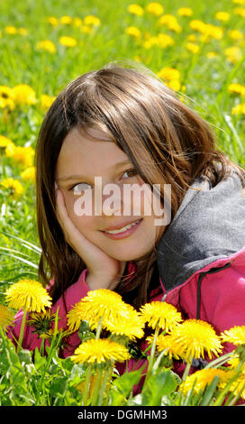 Ragazza, 12 anni, giacente in un campo di tarassaco, sorridente Foto Stock