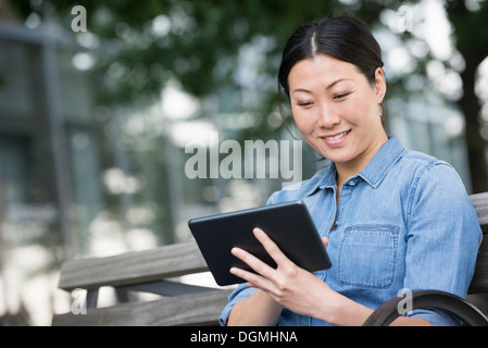 L'estate. Una donna seduta su una panchina utilizzando una tavoletta digitale. Foto Stock