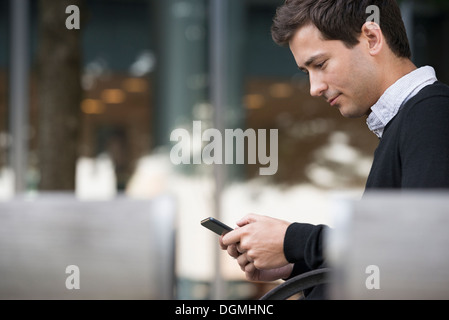 Estate in città. Un uomo seduto su un banco utilizzando un telefono intelligente. Foto Stock