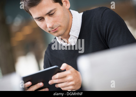 Estate in città. Un uomo seduto su una panchina utilizzando una tavoletta digitale. Foto Stock