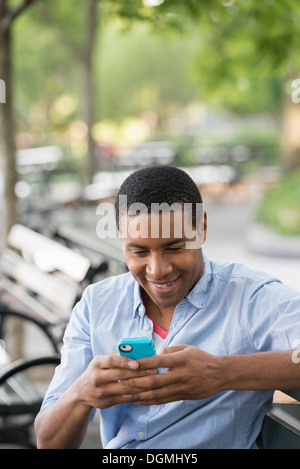 Estate in città. Un uomo seduto su un banco utilizzando un telefono intelligente. Foto Stock