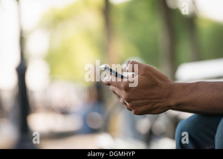 L'estate. Un uomo seduto su un banco utilizzando un telefono intelligente. Foto Stock