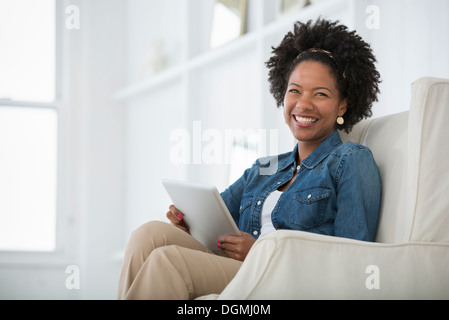 Una giovane donna seduta in una poltrona con una tavoletta digitale. Foto Stock