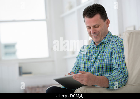 Un uomo seduto in poltrona, utilizzando una tavoletta digitale. Foto Stock