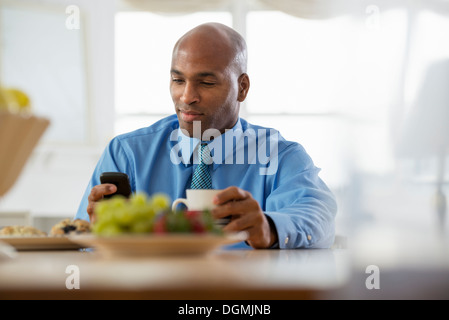 Un Uomo in camicia blu, seduto in un bar per la prima colazione con un telefono intelligente. Foto Stock