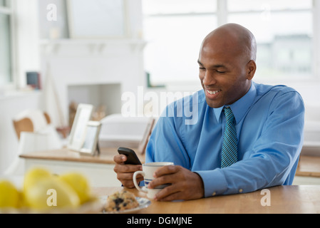 Un Uomo in camicia blu, seduto in un bar per la prima colazione con un telefono intelligente. Foto Stock