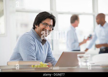 Vita in ufficio. Un giovane uomo seduto usando un computer portatile. Foto Stock