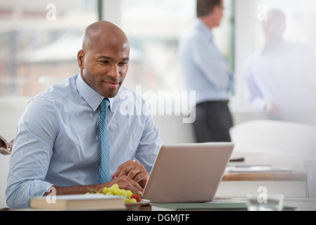 Vita in ufficio. Un imprenditore in una camicia e cravatta seduti ad una scrivania, utilizzando un computer portatile. Foto Stock