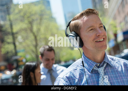 Un uomo che ascolta musica sul suo cuffie. Un paio in background. Foto Stock