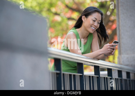 Una ragazza in un abito verde all'aperto in un parco della città sotto gli alberi in fiore. Foto Stock