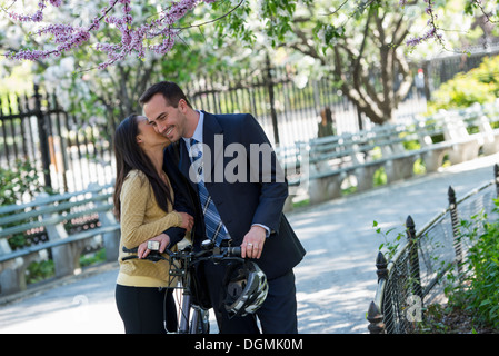 Un uomo in un business suit a cavallo di una bicicletta. Una donna baciare lui addio. Foto Stock
