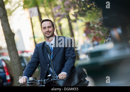 Un uomo in un business suit, all'aperto in un parco. Seduto su di una bicicletta. Foto Stock