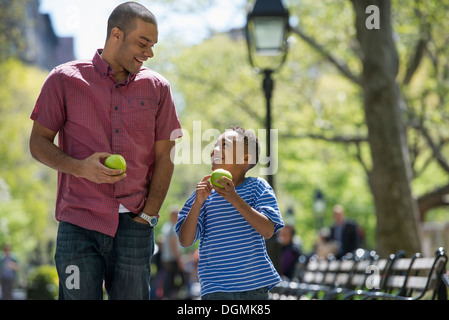 Una famiglia nel parco in una giornata di sole. Un uomo e un ragazzo di mangiare le mele. Foto Stock