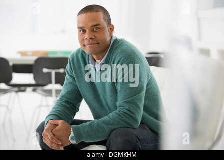 Business. Un uomo seduto e con le mani giunte in un rilassato fiducioso pongono. Foto Stock