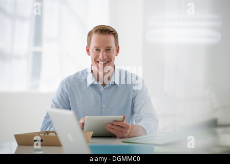 Business. Un chiaro e arioso ambiente office. Un uomo seduto in possesso di una tavoletta digitale. Foto Stock