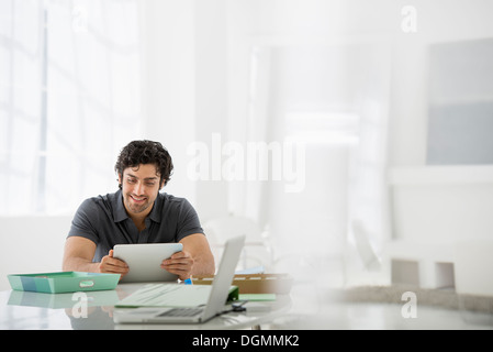 Business. Un chiaro e arioso ambiente office. Un uomo seduto in possesso di una tavoletta digitale. Foto Stock