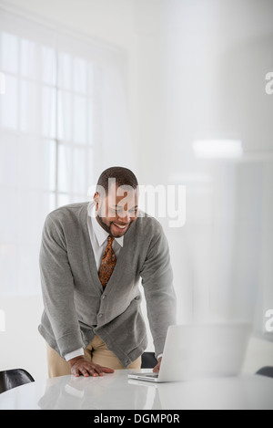 Ufficio interno. Un uomo in un business suit a una tabella. Utilizzando un computer portatile. Foto Stock