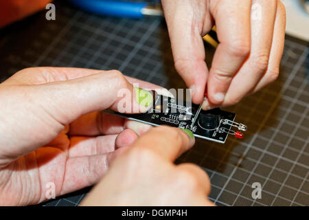 Mano con unghie verniciate e un bambino la mano lavorando insieme su un dispositivo elettronico con diodi emettitori di luce, IdeenPark 2012, Foto Stock