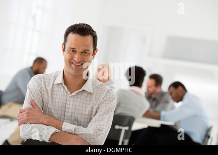 Ufficio interno. Un uomo seduto separatamente da un gruppo di persone sedute intorno ad un tavolo. Un incontro di affari. Foto Stock