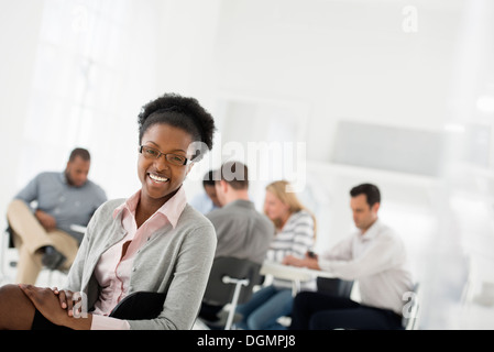 Ufficio interno. Un gruppo di persone in riunione. Una persona guardando sopra la sua spalla e lontano dal gruppo. Foto Stock