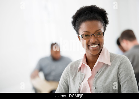 Ufficio interno. Una donna sorridente con fiducia. Due colleghi in background. Foto Stock