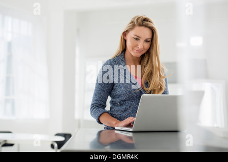 Ufficio interno. Una donna seduta a una tavola utilizzando una tavoletta digitale. Foto Stock