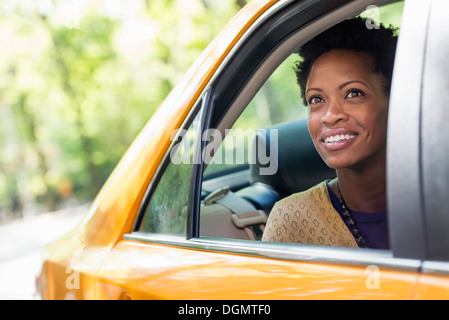 Una donna seduta nella parte posteriore del sedile passeggero di un taxi giallo. Foto Stock