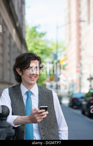 Un giovane uomo di affari sulla strada controllando il suo smart phone. Foto Stock