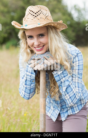 Sorridente donna bionda appoggiata su una pala indossando guanti da giardinaggio Foto Stock