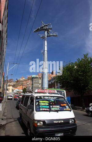 LA PAZ, BOLIVIA, 23 ottobre 2013. Un minibus di trasporto pubblico passa per uno dei piloni per la nuova funivia/cabinovia attualmente in costruzione per collegare le città di la Paz ed El alto. Il sistema è stato costruito dalla società austriaca Doppelmayr al costo di 234,6 milioni di dollari finanziati dal governo boliviano. Crediti: James Brunker/Alamy Live News Foto Stock