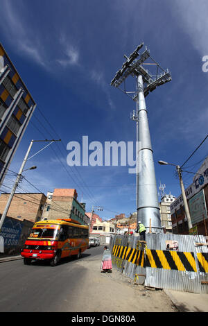 LA PAZ, BOLIVIA, 23 ottobre 2013. Un micro autobus pubblico rosso passa per uno dei piloni per la nuova funivia/cabinovia attualmente in costruzione per collegare le città di la Paz ed El alto. Il sistema è stato costruito dalla società austriaca Doppelmayr al costo di 234,6 milioni di dollari finanziati dal governo boliviano. Crediti: James Brunker/Alamy Live News Foto Stock