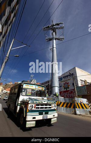 LA PAZ, Bolivia, 23 Ott, 2013. Un micro bus pubblico passa uno dei piloni per la nuova cabinovia / telecabina attualmente in costruzione per il collegamento delle città di La Paz e El Alto. Il sistema è stato costruito dalla società austriaca Doppelmayr ad un costo di $234.6 milioni di euro finanziati dal governo boliviano. Credito: James Brunker/Alamy Live News Foto Stock