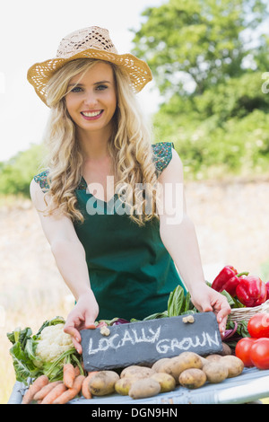 Sorridente femmina giovane agricoltore in piedi alla sua pressione di stallo Foto Stock