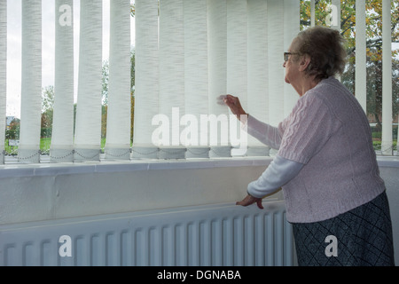 Donna di novanta anni con mano sul radiatore che guarda fuori dalla finestra. REGNO UNITO. Coronavirus, autoisolamento, distanza sociale, quarantena... concetto Foto Stock