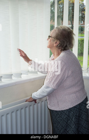 Donna di novanta anni con mano sul radiatore che guarda fuori dalla finestra. REGNO UNITO. Coronavirus, autoisolamento, distanza sociale, quarantena... concetto Foto Stock