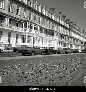 Alla fine degli anni '60, immagine storica di una fila di grandi case a schiera georgiane a cinque piani a Brighton, E. Sussex, Inghilterra, Regno Unito, con auto dell'epoca parcheggiate di fronte alla strada. Foto Stock