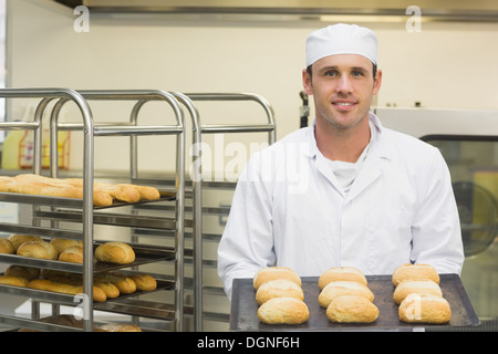 Felice giovani baker holding alcuni rotoli su un vassoio da forno Foto Stock