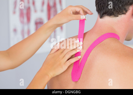 Fisioterapista mettendo in rosa kinesio nastro su pazienti maschi collo Foto Stock