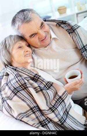 Ritratto di serena coppia senior avvolti in plaid avente il resto a casa Foto Stock