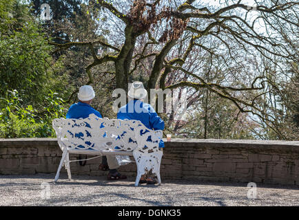 Coppia senior seduta su una panchina in un parco di Mainau, Baden-Württemberg, Germania Foto Stock
