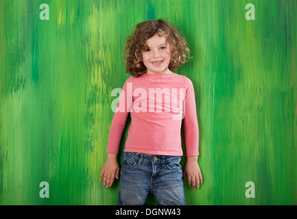 I Capelli rossi ragazza, 5 anni, in piedi di fronte a un muro verde Foto Stock