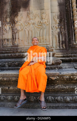 Monaco buddista nel centro di Angkor Wat seduto davanti a un rilievo raffigurante Apsara dalla mitologia indù, Cambogia Foto Stock