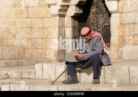 Uomo palestinese con keffiyeh o kafiya seduta sul suo proprio sui gradini della porta di Damasco, città vecchia, Gerusalemme, Israele Foto Stock