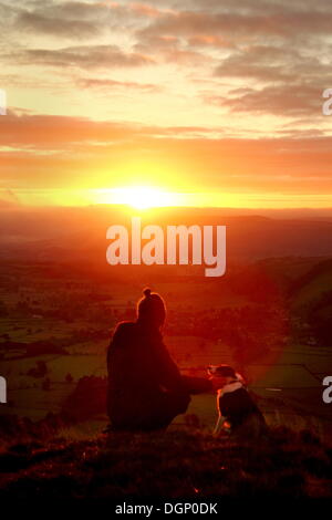 Walker con cane testimonianza tramonto sull'Hope Valley da Mam Tor; un punto di riferimento collina vicino Castleton nel Parco Nazionale di Peak District, DERBYSHIRE REGNO UNITO Inghilterra Foto Stock