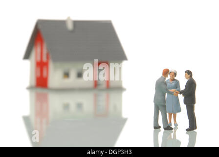 Matura per comprare una casa da un agente immobiliare, figurine, una casa sfocata nel retro, immagine simbolica per il mercato immobiliare Foto Stock